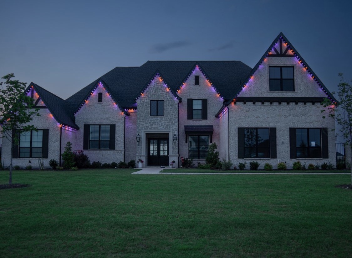 Purple and orange lighting tracing the roofline of a brick home