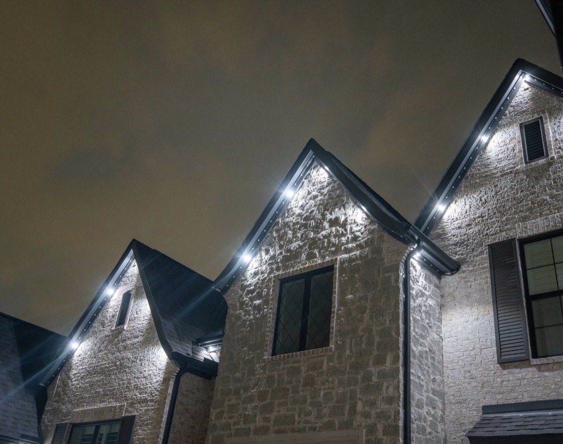 White permanent light modules accenting stone gables at night